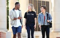 Three students smiling and talking walking outside of 默尔顿塔.